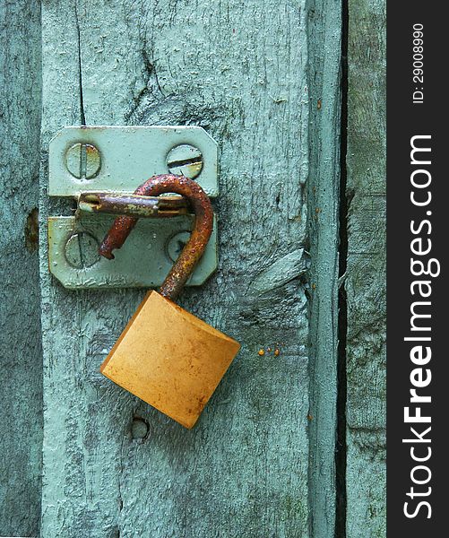 A rusty brass lock hangs on a steel hasp on a green door. A rusty brass lock hangs on a steel hasp on a green door