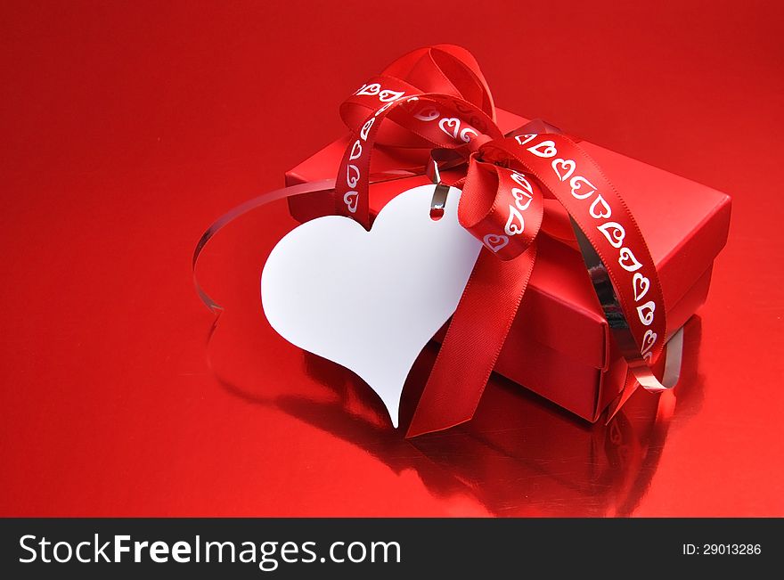 Red present gift with white heart shaped gift tag and ribbons and bow on a red background, for Valentine's Day or someone special. Red present gift with white heart shaped gift tag and ribbons and bow on a red background, for Valentine's Day or someone special.