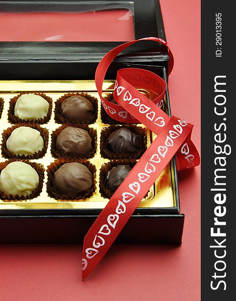Beautiful Valentine black and gold box of delicious white, milk and dark chocolates in a black and gold box with romantic red heart ribbon on a red background. Beautiful Valentine black and gold box of delicious white, milk and dark chocolates in a black and gold box with romantic red heart ribbon on a red background.