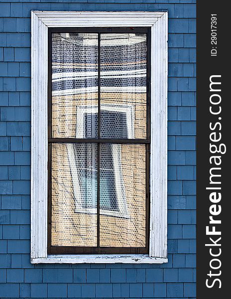 Window in a blue wooden shingled house reflects the window of a yellow wooden shingled house across the street. Window in a blue wooden shingled house reflects the window of a yellow wooden shingled house across the street.