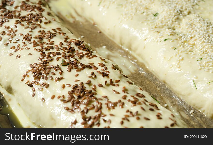 Meatloaf made from yeast dough sprinkled with flax and sesame seeds on parchment. Ready to bake, close-up, macro