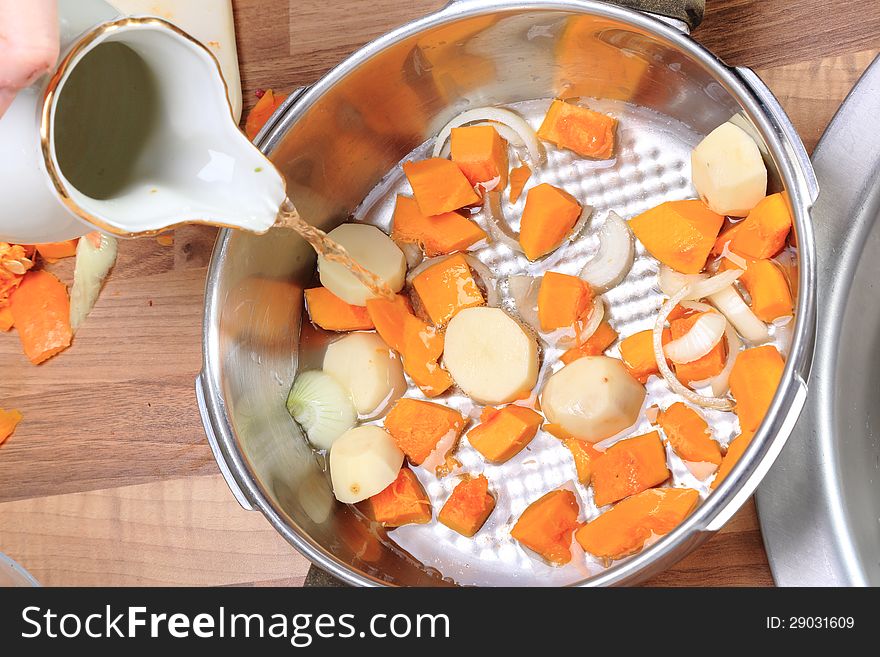 Making a pumpkin soup:Pieces of a red pumpkin and of potatoes with some slices of onion in a pressure cooker. Water is added. Making a pumpkin soup:Pieces of a red pumpkin and of potatoes with some slices of onion in a pressure cooker. Water is added.