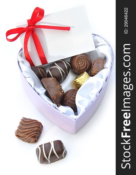 Assortment of chocolates inside a heartshaped box with a card and decorative red ribbon. Assortment of chocolates inside a heartshaped box with a card and decorative red ribbon