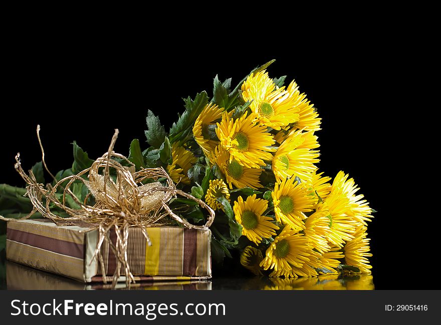 Bouquet of yellow chrysanthemums and gift box with bow on a black