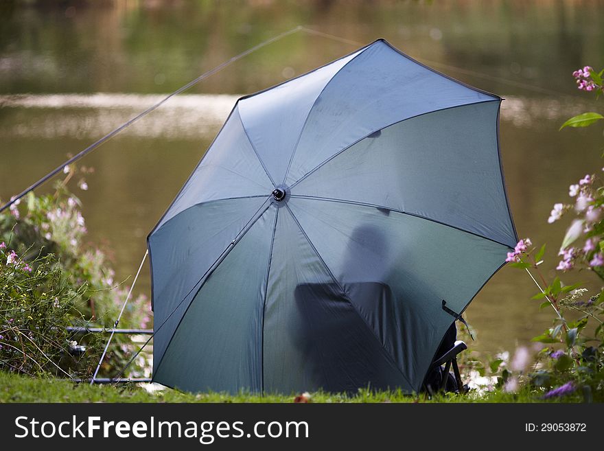 Person sheltered under an umbrella fishing in a lake. Person sheltered under an umbrella fishing in a lake