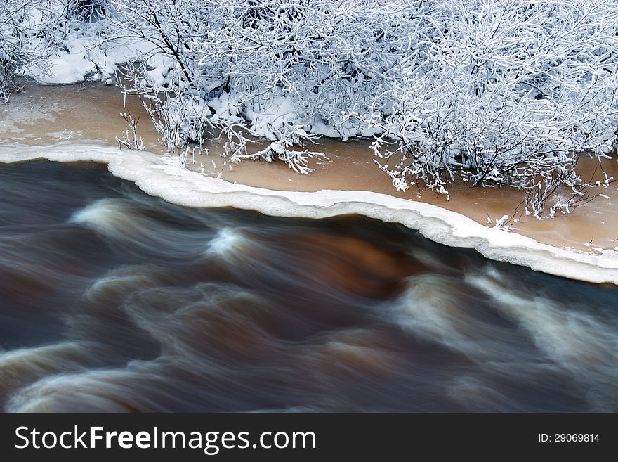 Water flow in river , edge of the ice and hoarfrost covered branches in winter evening. Water flow in river , edge of the ice and hoarfrost covered branches in winter evening