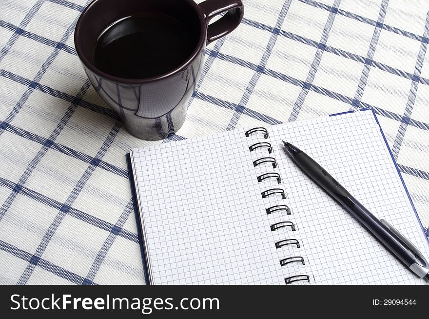 Notebook lying on the tablecloth next to a pen and a cup of coffee