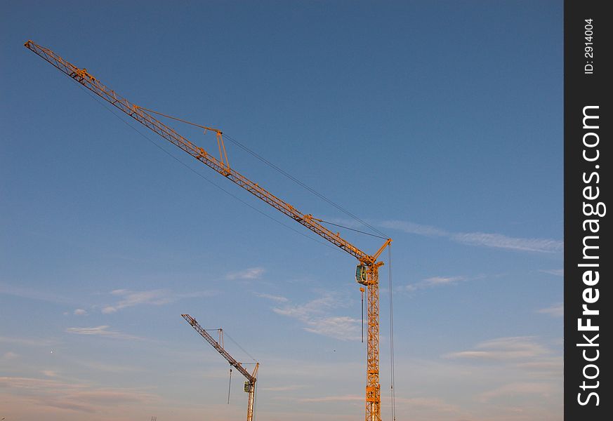 Two modern building cranes by the blue sky