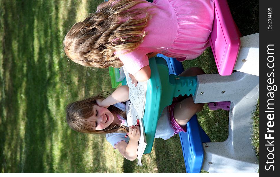 Two girls share some quiet time outside coloring and talking. Two girls share some quiet time outside coloring and talking