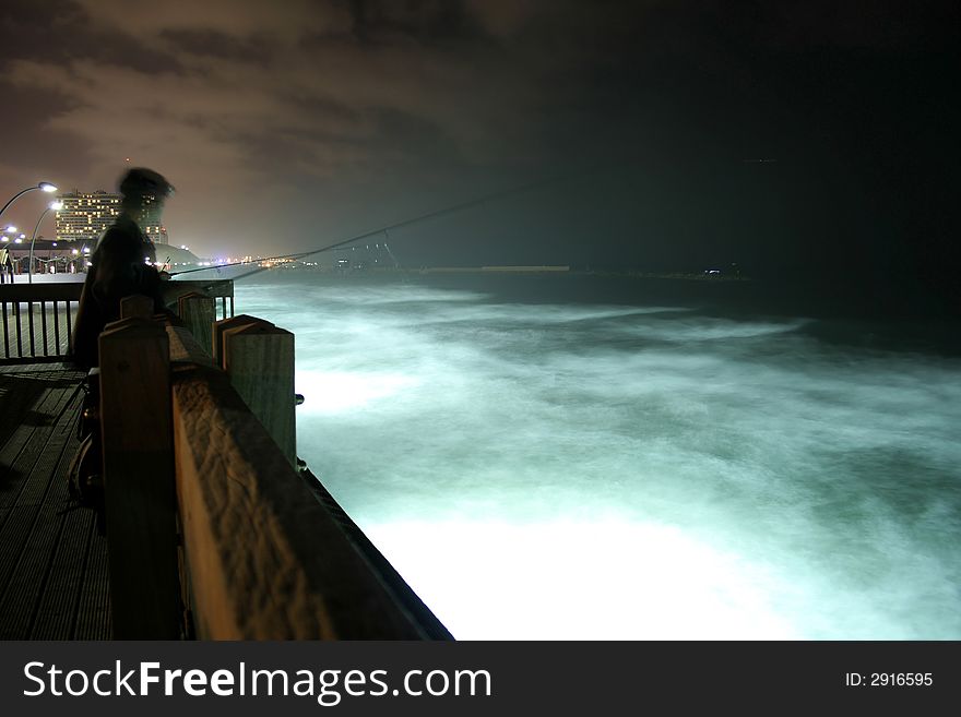 Fisherman on pier by night