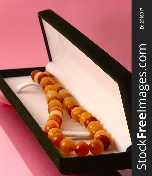 Amber beads in a box on a pink background. Amber beads in a box on a pink background