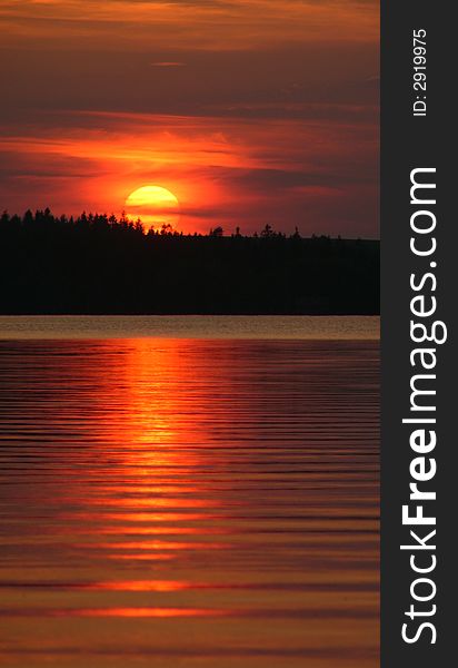 Picturesque red sunset silhouetting forest on coastline with lake or water in background. Picturesque red sunset silhouetting forest on coastline with lake or water in background.