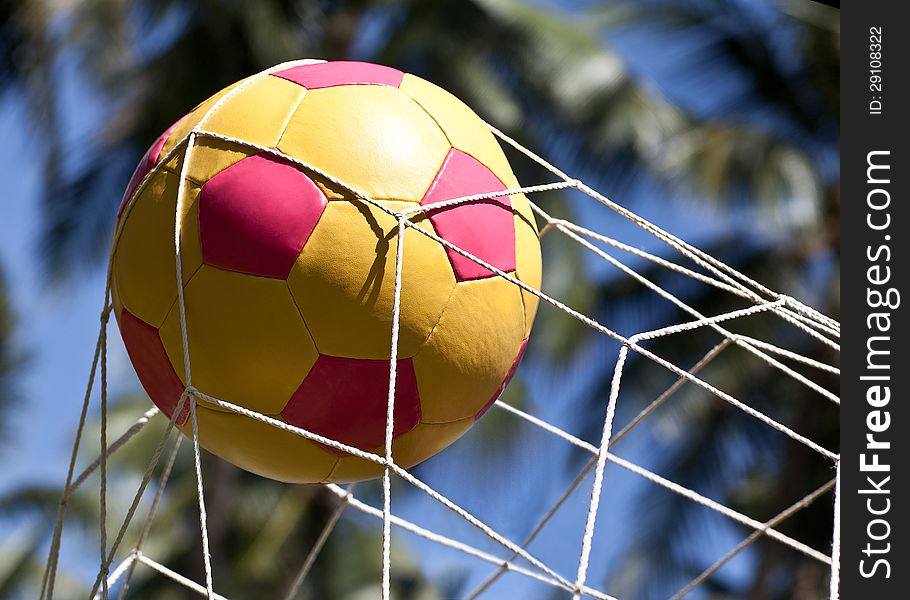 The soccer ball in the net gate on the background of blue sky and palm trees. The soccer ball in the net gate on the background of blue sky and palm trees