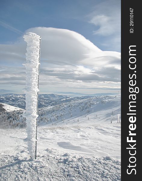 Top of the mountain in winter with iron pillar covered by icicles and white clouds on blue sky. Top of the mountain in winter with iron pillar covered by icicles and white clouds on blue sky