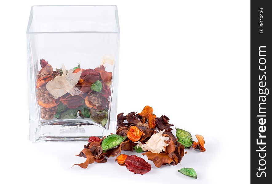 Colorful natural pot pourri with dried seasonal flowers, leaves and spices on a white background alongside a half full glass container for a scented fragrance in the house