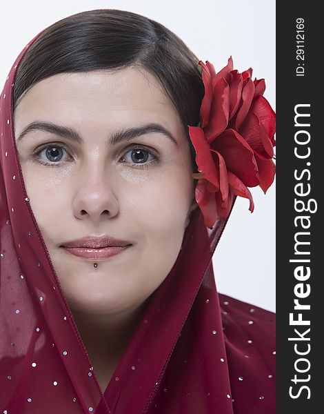 Closeup portrait of young brunette woman with big red rose and wrap on her head. Closeup portrait of young brunette woman with big red rose and wrap on her head