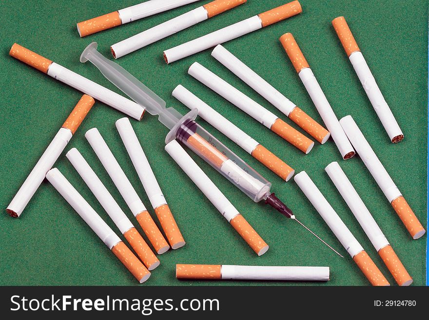 Nicotine dependence. metaphor syringe loaded cigarette and a few cigarettes lying on a green surface.