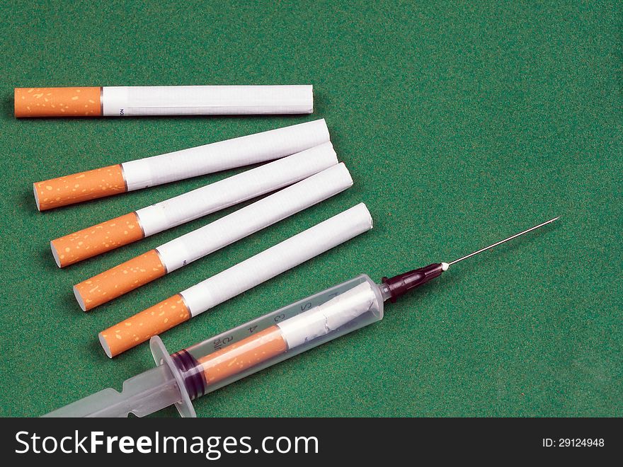 Nicotine dependence. metaphor syringe loaded cigarette and a few cigarettes lying on a green surface.