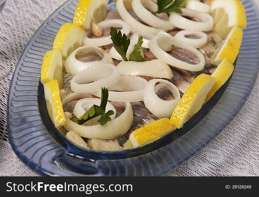 Salted herring with onion and lemon on table.