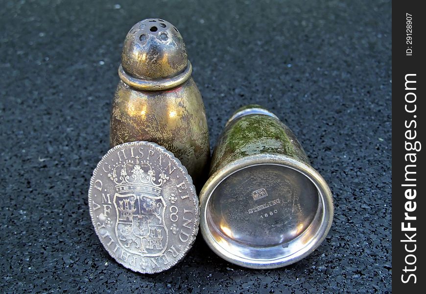 Antique silver salt and pepper shakers and an old Spanish coin on a black background. Antique silver salt and pepper shakers and an old Spanish coin on a black background.