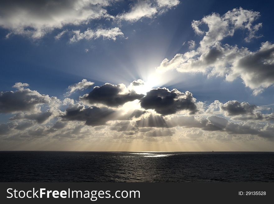 Light rays shine through the group of clouds in the middle of the ocean