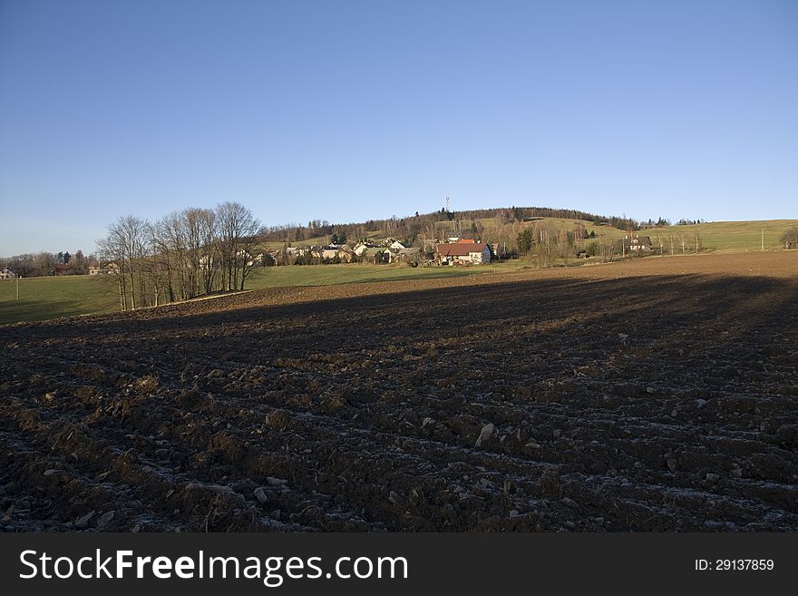 Plowed field in the shadow in the background with the village. Plowed field in the shadow in the background with the village