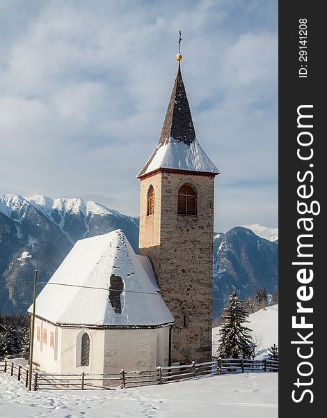 A wintertime view of a small church with a tall steeple in Montassilone, Sud Tyrol