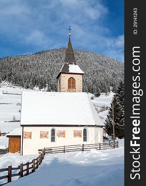 A wintertime view of a small church with a tall steeple in Vila di Sopra, Sud Tyrol