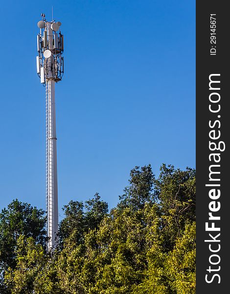 Telecommunication mast and green trees at the blue sky