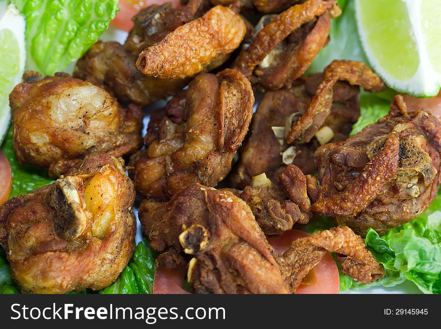 Fried chicken parts with bone on a bed of tomato and lettuce with a slice of lime.