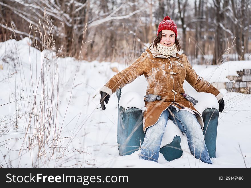 Young girl with red hat sitting on the arm-chair outside, outdoor portrait on a winter day