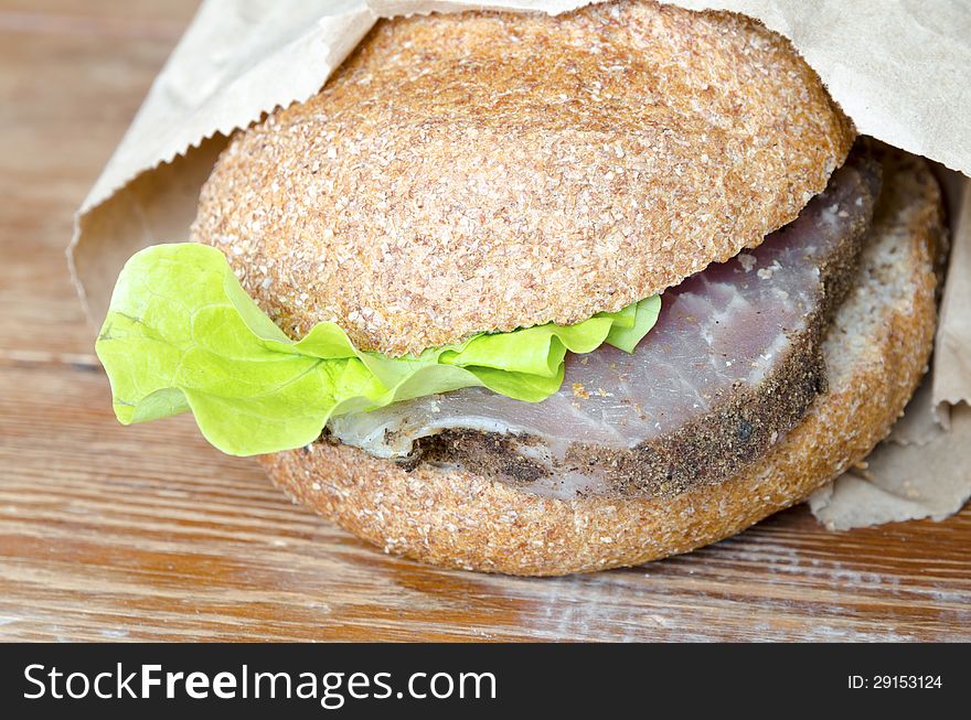 Fresh burger with paper wrapping on the rough wooden surface. Fresh burger with paper wrapping on the rough wooden surface