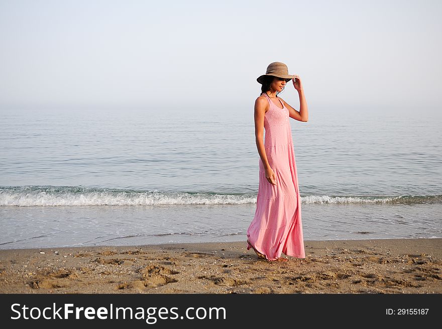 Portrait of a beautiful woman with long pink dress and sun hat on a tropical beach. Portrait of a beautiful woman with long pink dress and sun hat on a tropical beach