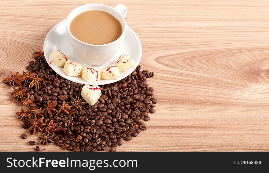 Cup of coffee with beans and white chocolate heart candy  over wooden background