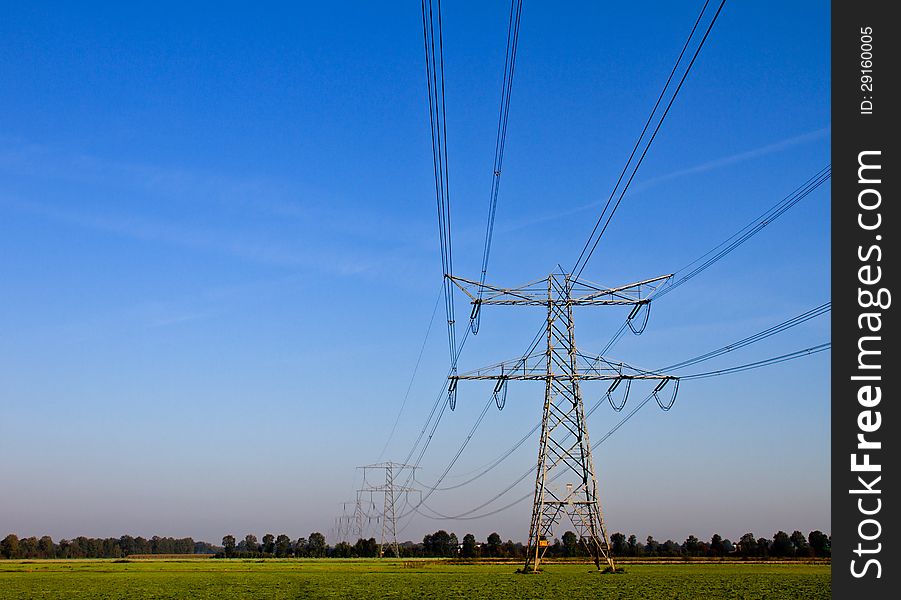 A lush field with electricity pylons and trees in background on a hot summers day. A lush field with electricity pylons and trees in background on a hot summers day.