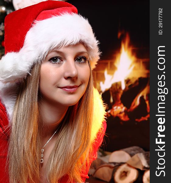 Portrait of beautiful girl wearing Santa Claus clothes and fireplace as a background. Portrait of beautiful girl wearing Santa Claus clothes and fireplace as a background