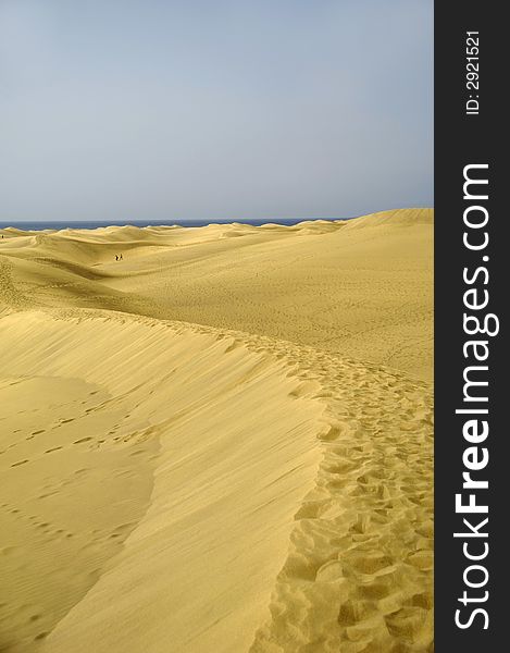 Landscape with sand dunes and people and ocean in the background.