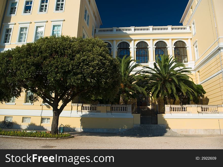 Yellow historical building of school, with trees and palms,  dark blue sky, Zadar, Croatia