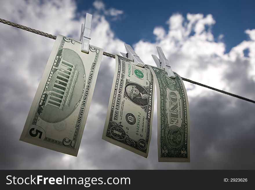 US dollar notes on a clothesline. A dramatic sky is visible as background. US dollar notes on a clothesline. A dramatic sky is visible as background.