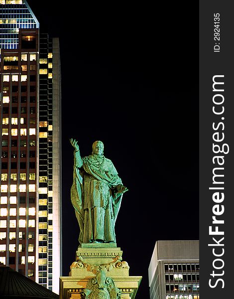 Monseigneur Bourget statue on the backdrop of skyscrapers in Montreal at night.