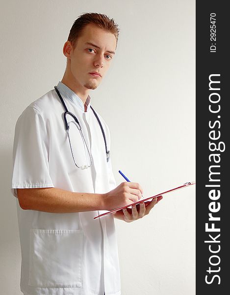 Young doctor writing with a red clipboard in his hands. Young doctor writing with a red clipboard in his hands