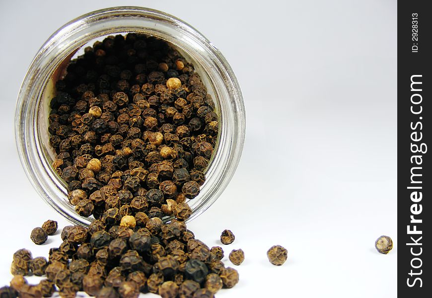 Whole black pepper in a bottle, isolated on white.