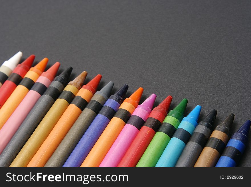 Brightly colored crayons lined up on black paper. Brightly colored crayons lined up on black paper.