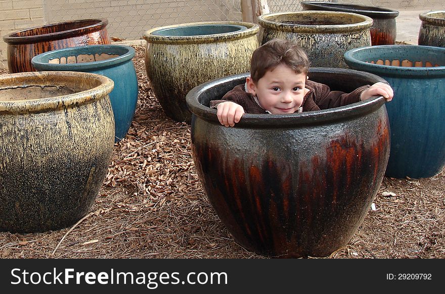 Little boy peeking out of the flower pot sitting in the midst of the pots. Little boy peeking out of the flower pot sitting in the midst of the pots