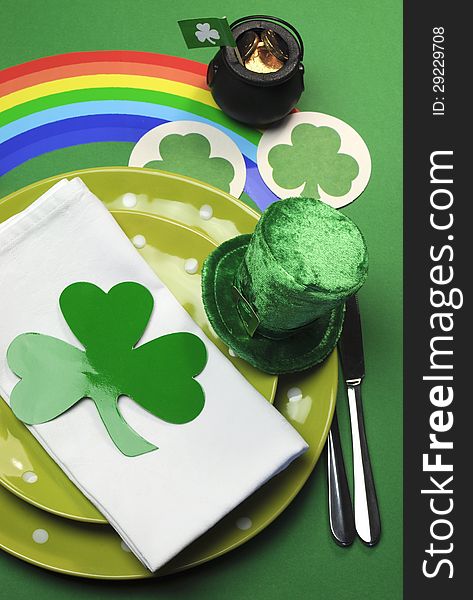 St Patrick's Day party table setting decorated with green polka dot plates, shamrocks, pot of gold and leprechaun hat with rainbow on green background. St Patrick's Day party table setting decorated with green polka dot plates, shamrocks, pot of gold and leprechaun hat with rainbow on green background.