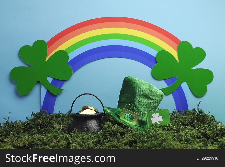 St Patrick's Day still life with leprechaun hat, pot of gold, shamrocks and rainbow on blue background with green grass moss. St Patrick's Day still life with leprechaun hat, pot of gold, shamrocks and rainbow on blue background with green grass moss.