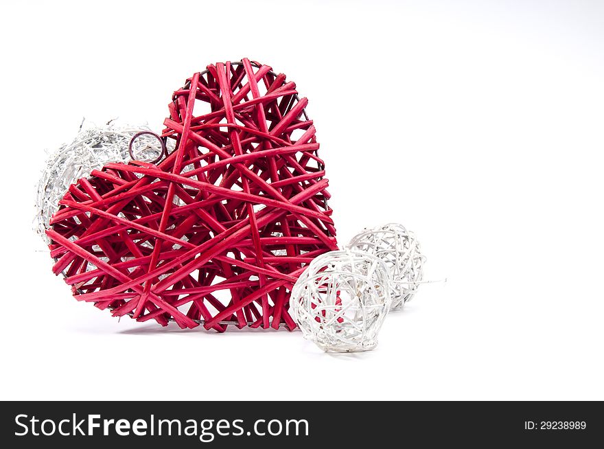 Red wicker heart resting on small white wicker balls at an angle on white background