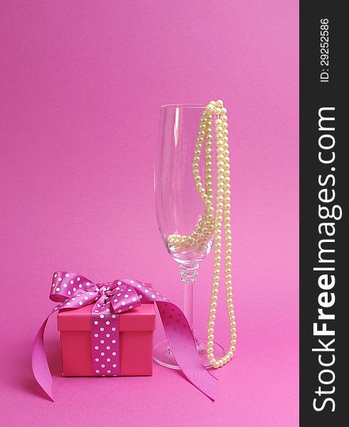 Pretty pink and feminine gift with polka dot pink ribbon and a champagne glass with pearls against a pink background.