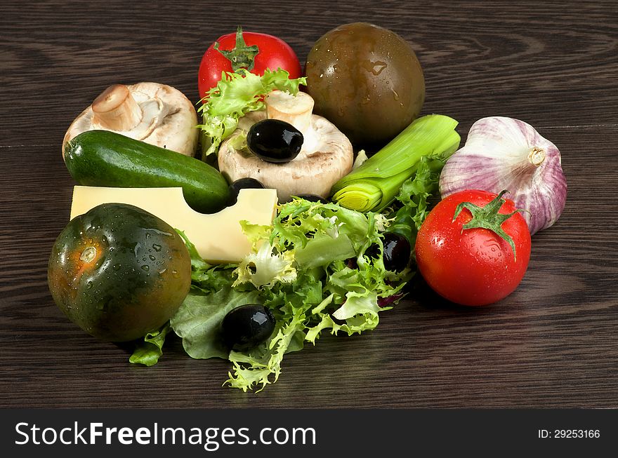 Arrangement of Red an Green Tomatoes, Lettuce, Leek, Raw Mushrooms, Black Olives, Cheese, Cucumber and Garlic closeup on Dark Wood background. Arrangement of Red an Green Tomatoes, Lettuce, Leek, Raw Mushrooms, Black Olives, Cheese, Cucumber and Garlic closeup on Dark Wood background