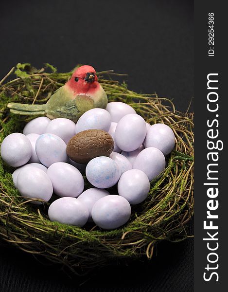 Close-up of chocolate Easter egg among sugar coated candy marble eggs in moss birds nest against a black background. Vertical portrait orientation. Close-up of chocolate Easter egg among sugar coated candy marble eggs in moss birds nest against a black background. Vertical portrait orientation.